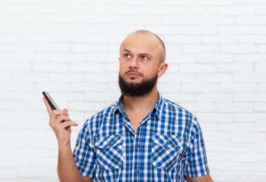 Man Holding phone with collared blue plad shirt on, white brick background