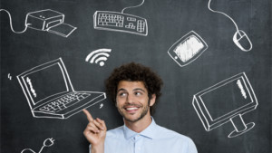 Person pointing at Laptop with varying technology behind on blackboard