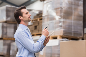 Man in blue collared shirt pointing upwards to right with warehouse boxes behind