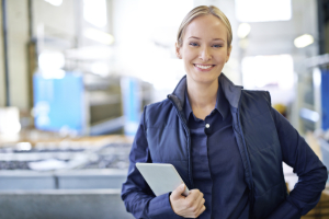 Woman Holding notepad facing toward camera in blue shirt and vest, blurred office in background