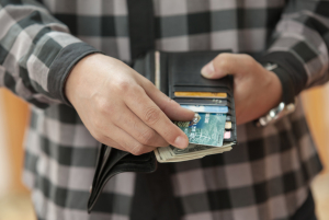 Hands taking credit card out of black wallet with plad shirt