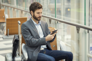 Man(in suit) in airport looking at phone while sitting
